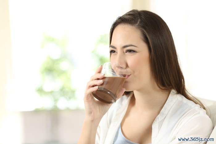 Happy woman drinking a cocoa shake sitting on a couch in the living room at home